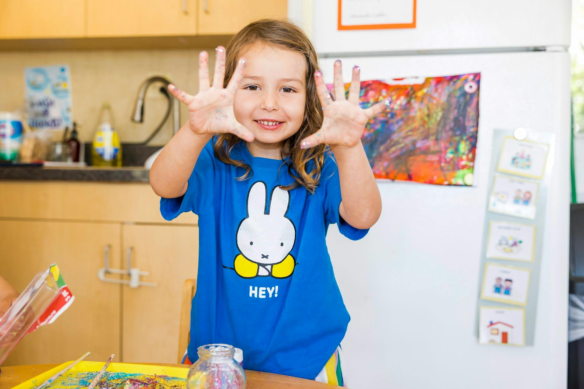 Child in a blue shirt holding up both hands
