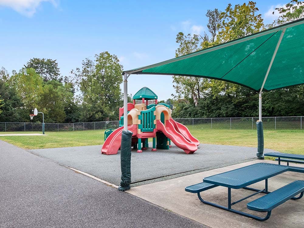 Playground with slides, basketball hoop, and picnic tables under a shade canopy