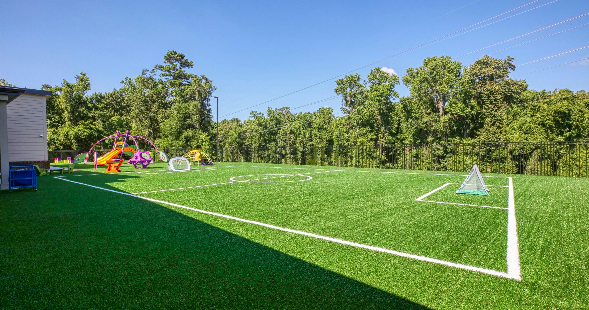Fenced playground with artificial grass field and colorful equipment