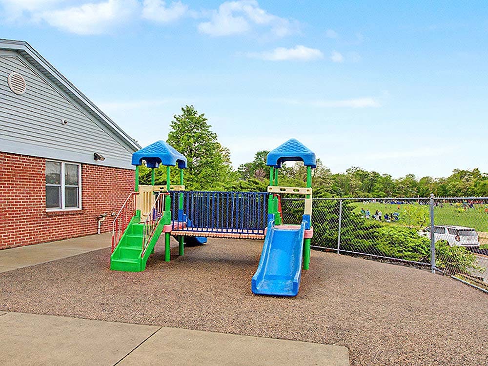 Playground with slides and stairs next to a building and fenced field