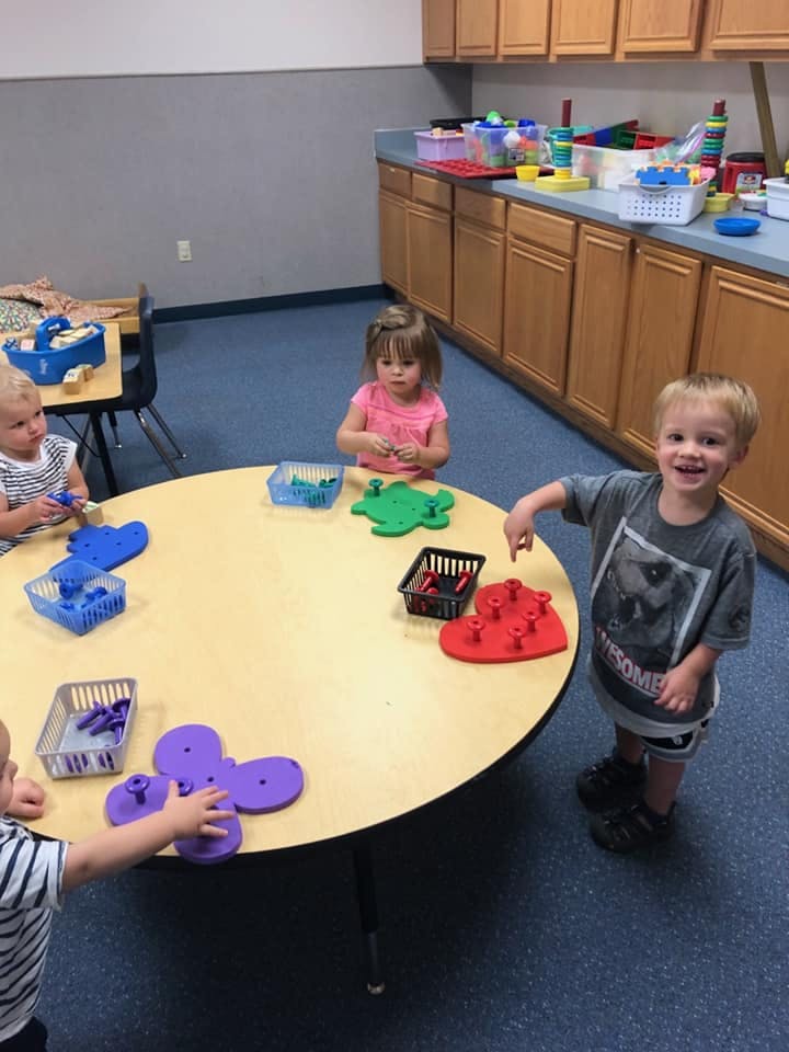 Children playing with toys at a round table in a classroom