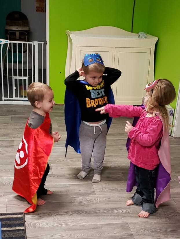 Three children in superhero capes and masks playing indoors