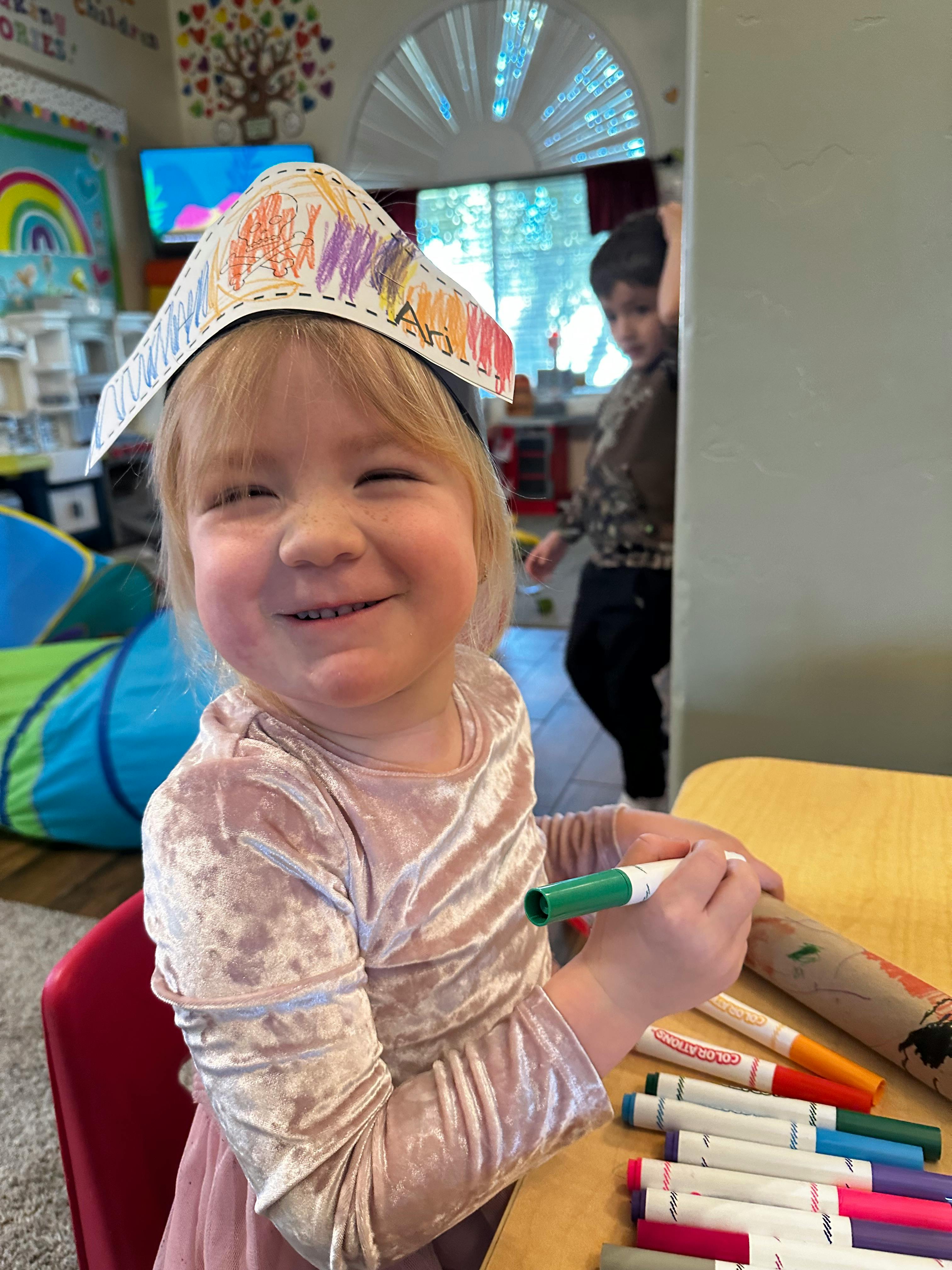 Child wearing a paper crown and holding a green marker