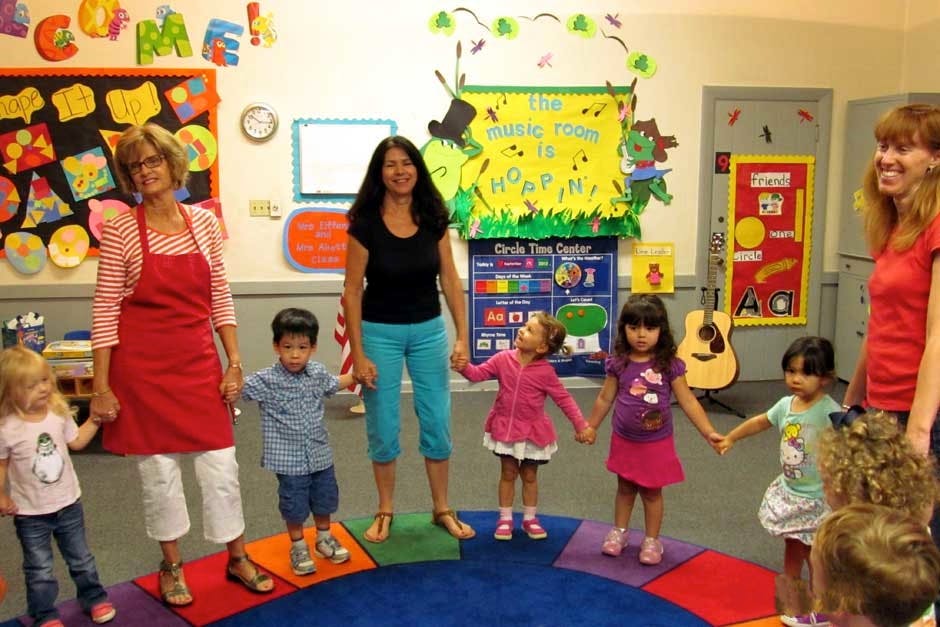 Adults and children holding hands in a circle in a classroom
