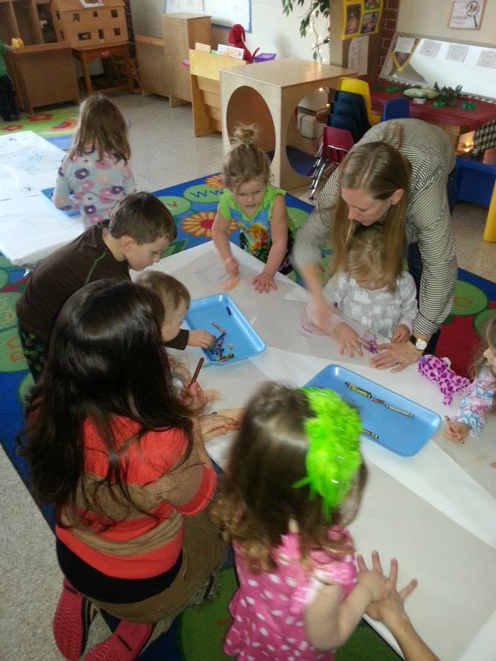 Adult and children on floor drawing on paper