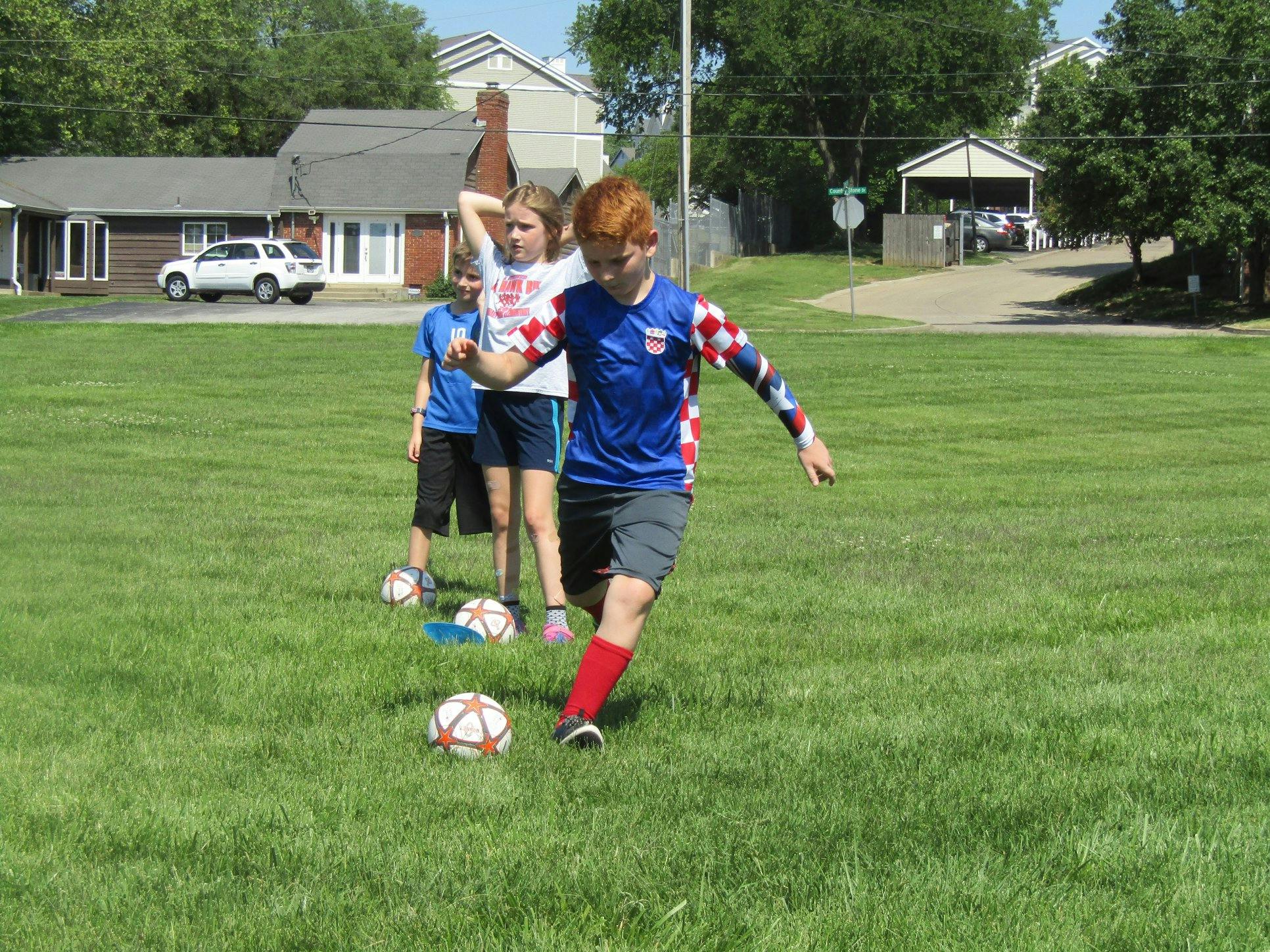 Child in blue shirt kicking a soccer ball with other children in background