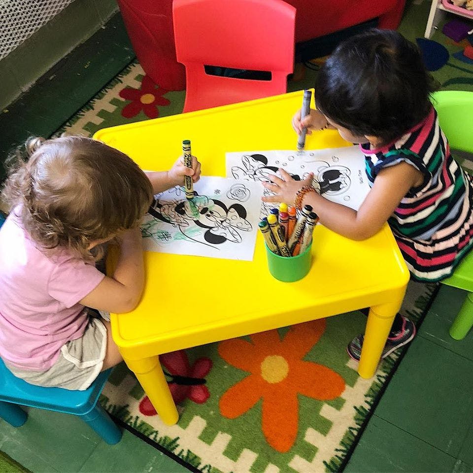 Two children coloring at a yellow table