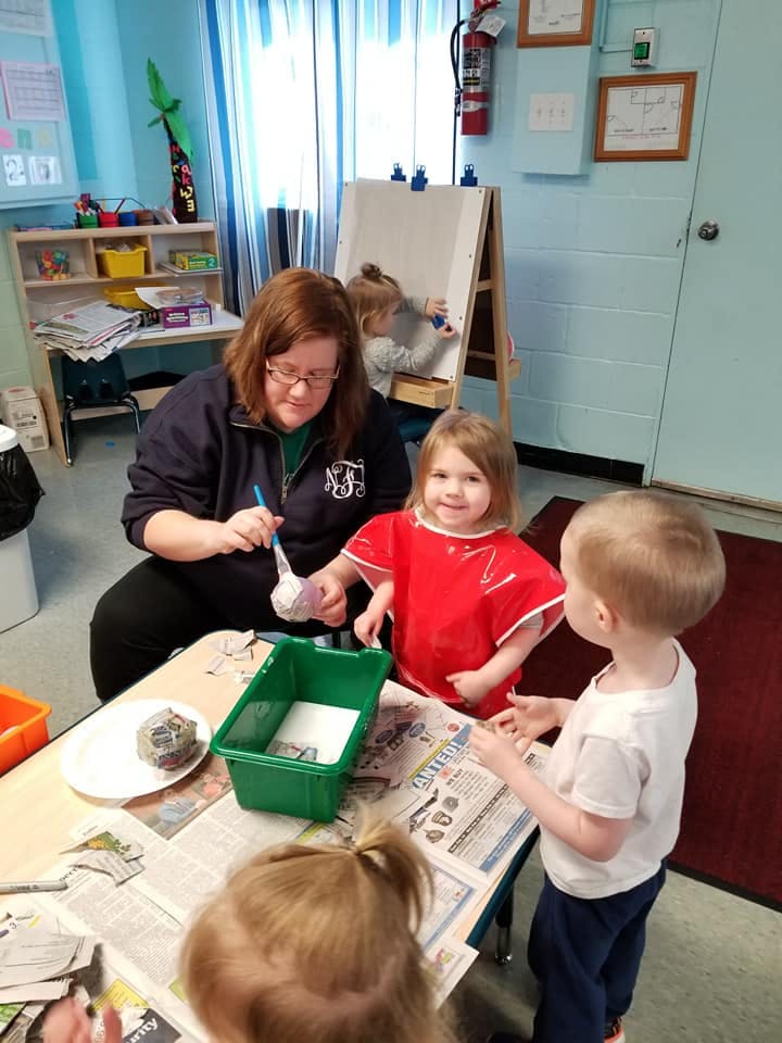 Adult and two children doing an art activity at a table in a classroom