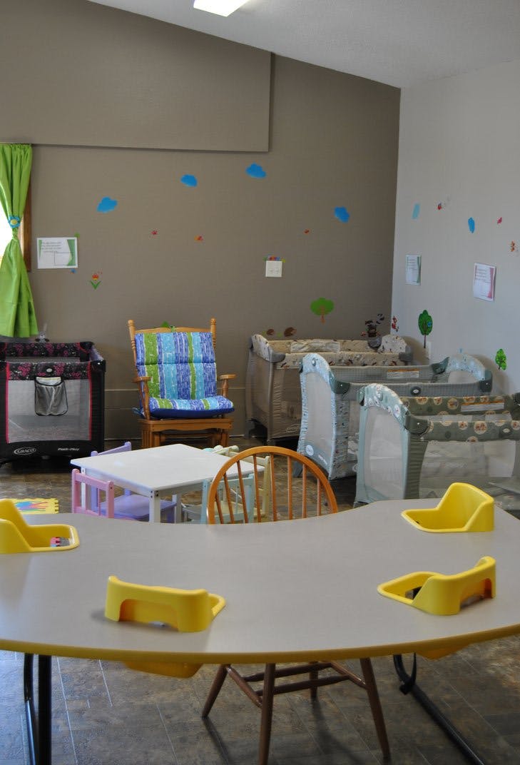Daycare room with cribs, small tables, and chairs