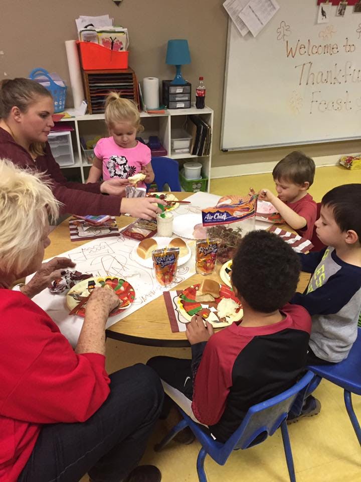 Adults and children sitting around a table eating in a classroom