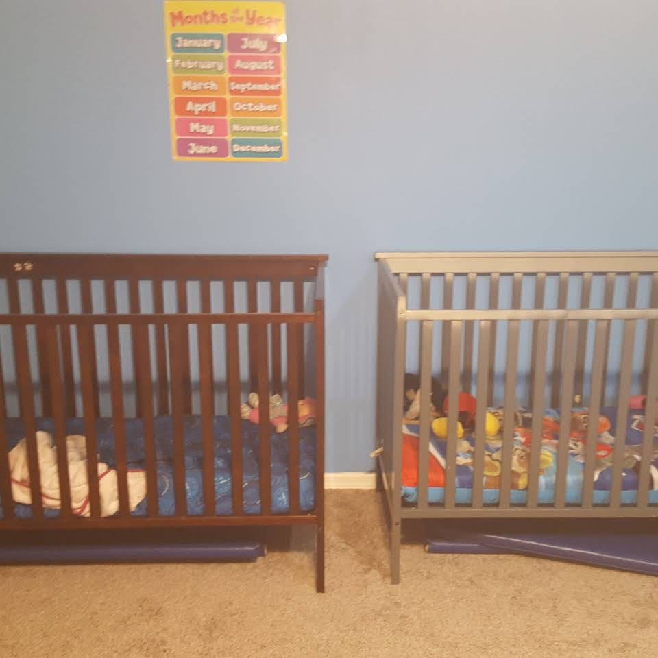 Two cribs in a room with a colorful months of the year chart on the wall