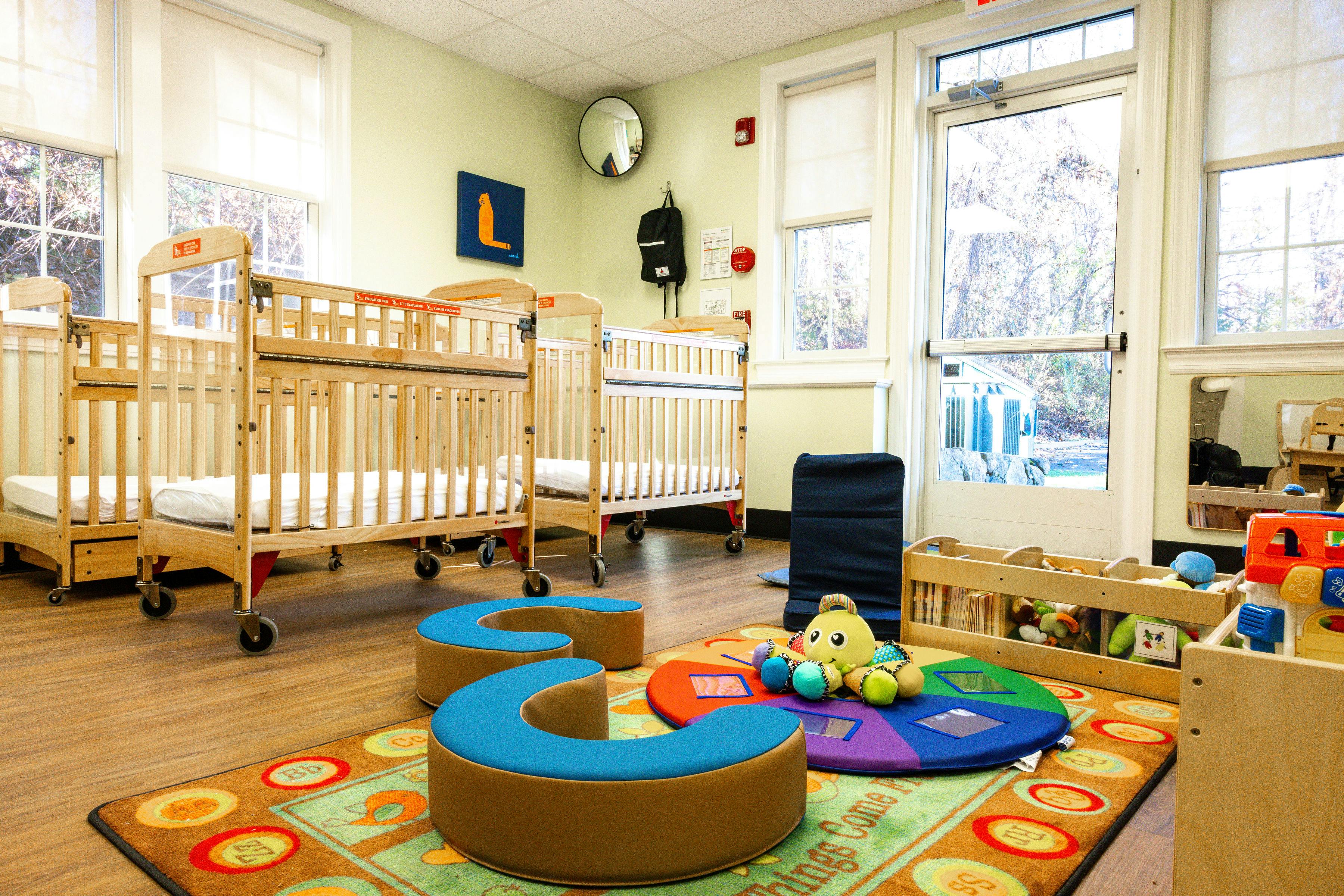 cribs in a bright room with a colorful play rug and toys