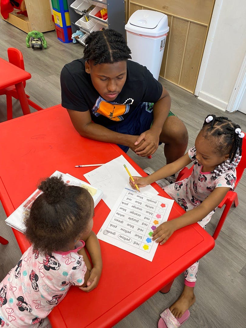 Person and two children at a red table with papers and pencils