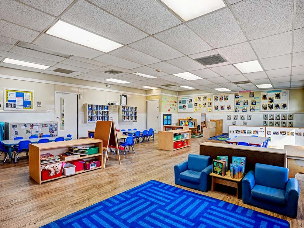 Classroom with small tables and chairs, toys, and a blue rug