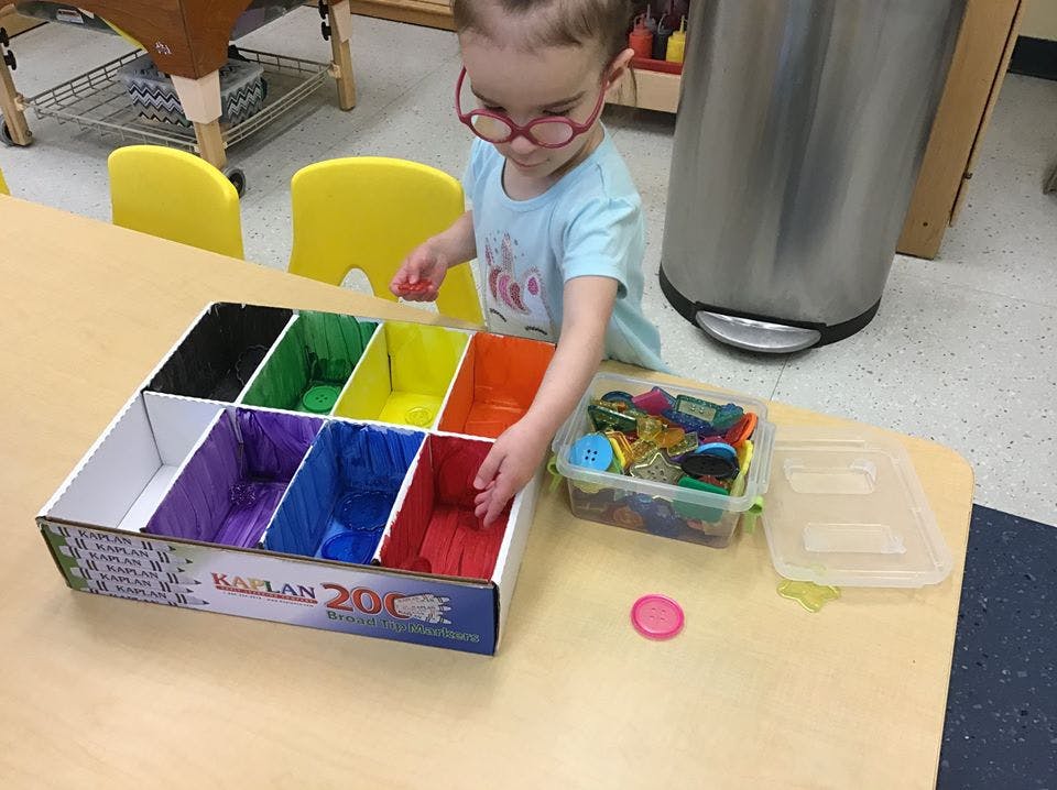 Child sorting items into a multi-colored organizer on a table