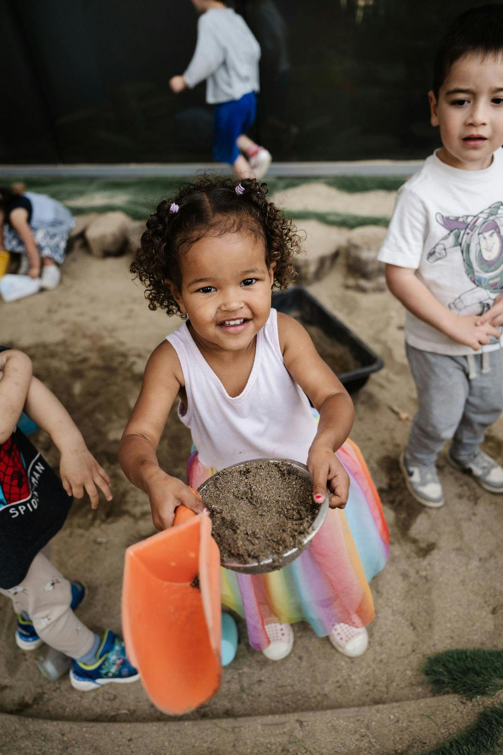 Child holding a bowl of sand and a shovel in a sandbox