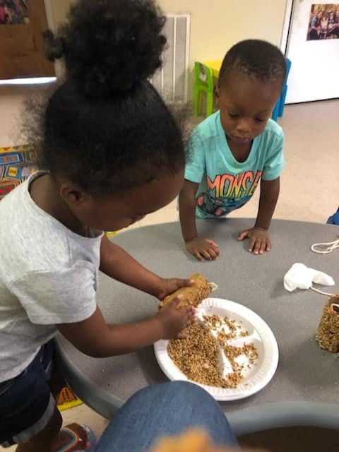Child pressing food into a plate while another child watches