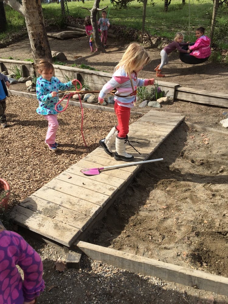 Child walking on a wooden plank, another child holding a rope