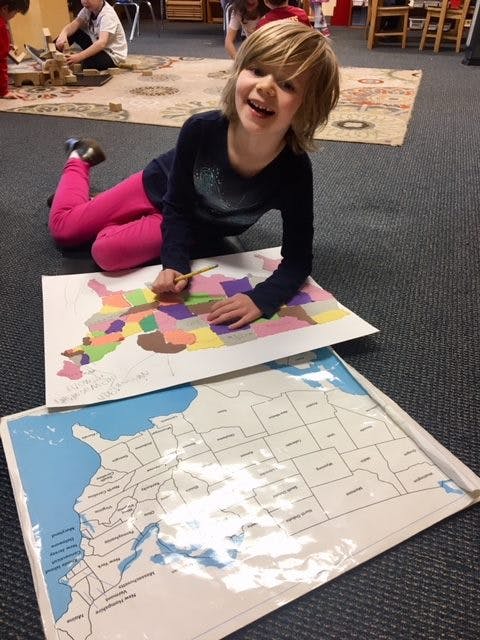 Child coloring a map of the United States on the floor