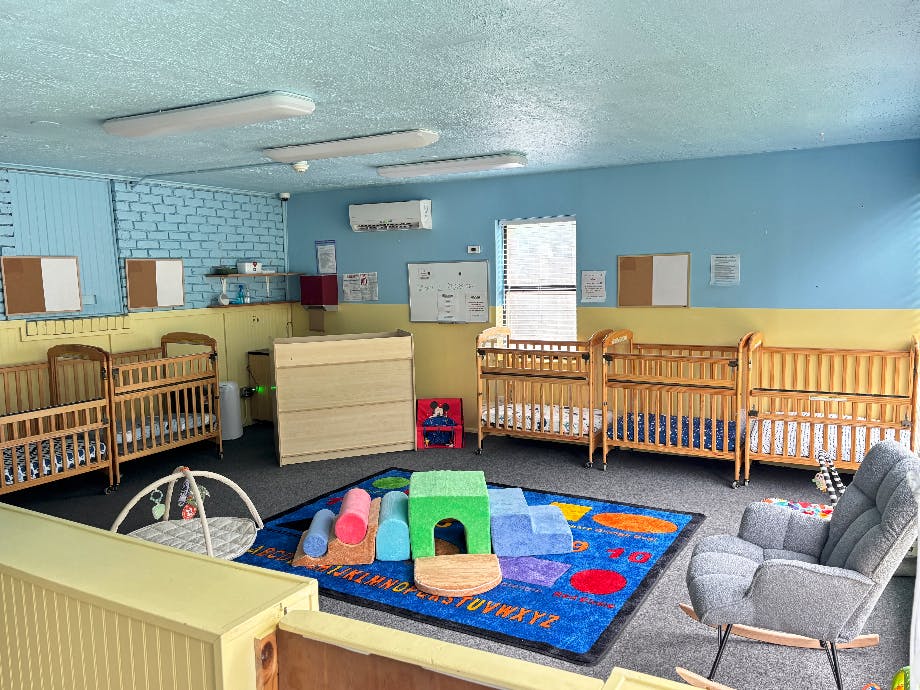 Group of wooden cribs in a daycare room with a colorful play rug