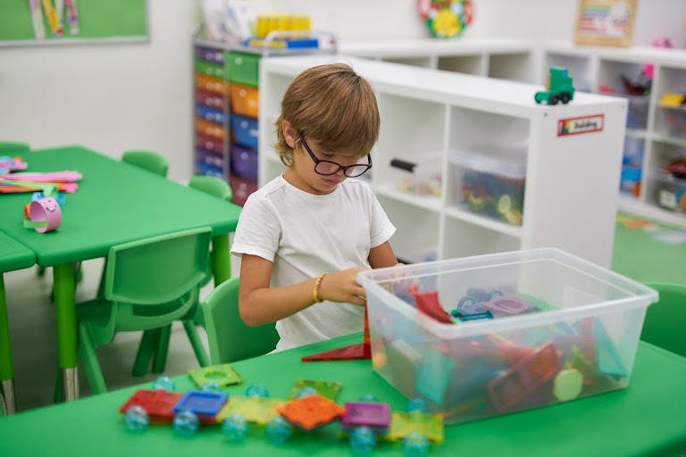 Child with glasses playing with building blocks in a classroom