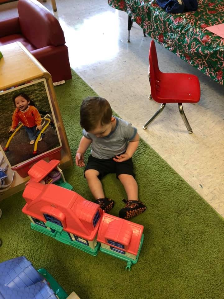 Child sitting on a green rug next to a toy train