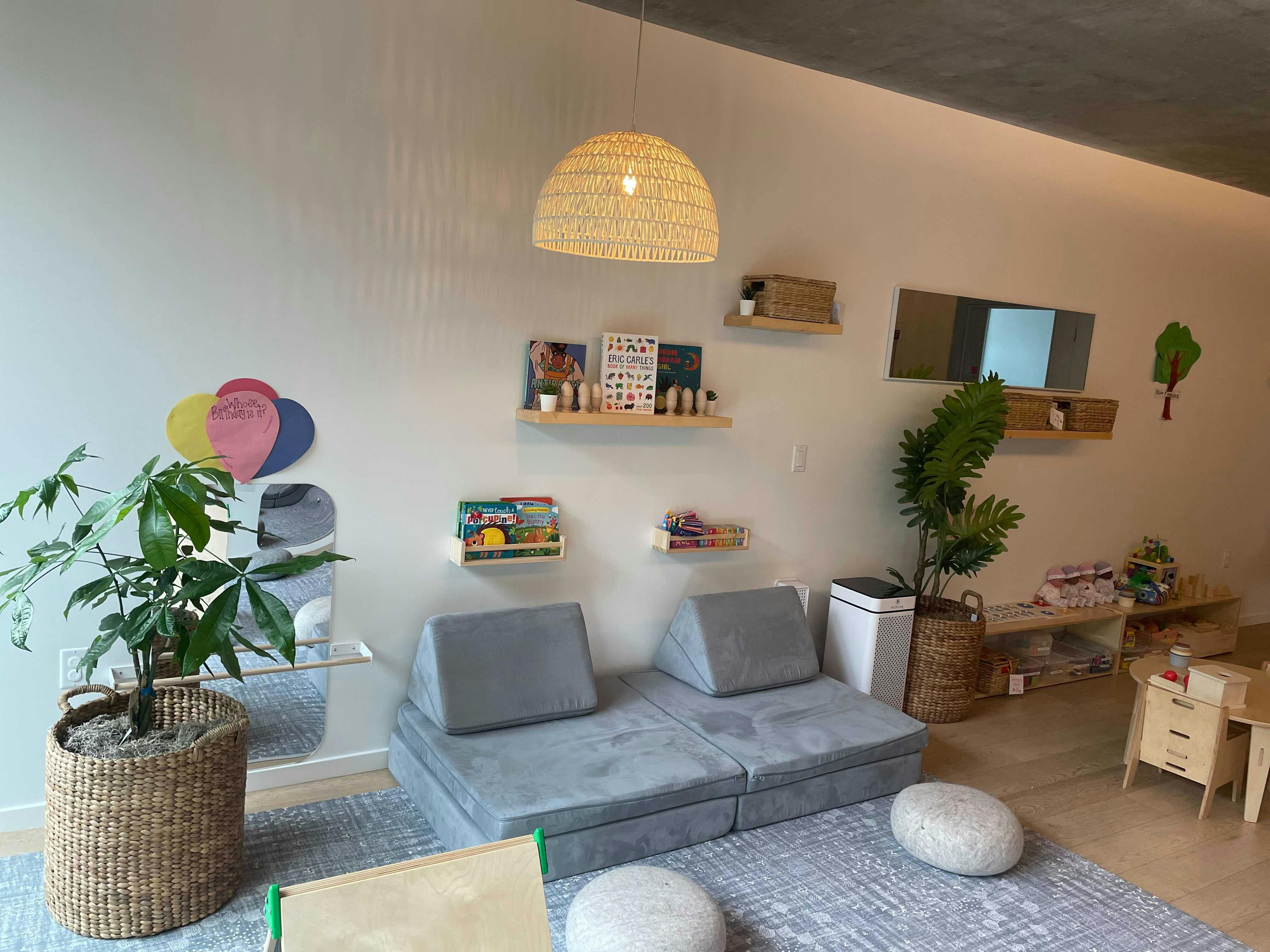 Playroom with a gray modular sofa, shelves with books, and plants