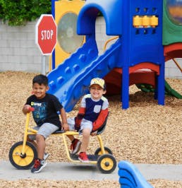 Two children sitting on a yellow tandem tricycle on a playground
