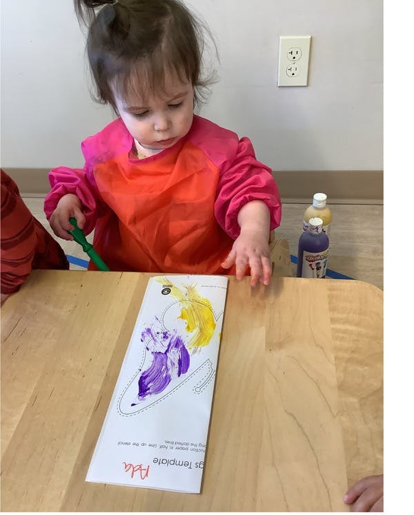 Child in a smock painting a template that says "Ada"