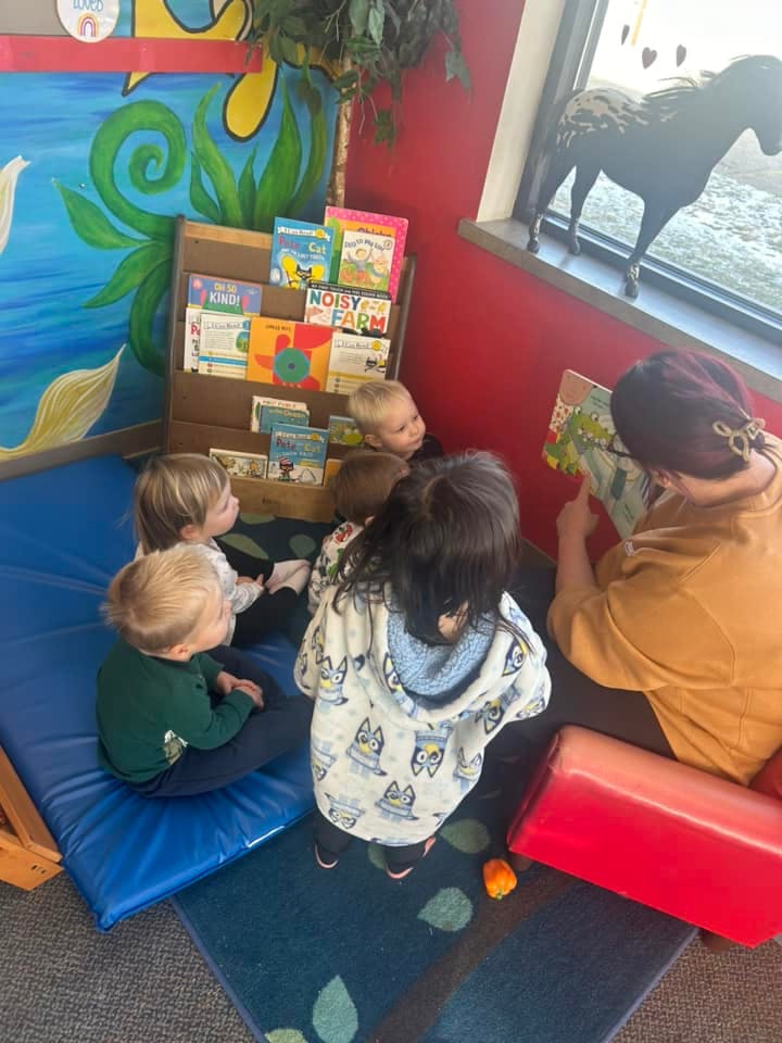 Adult reading a book to a group of children in a classroom