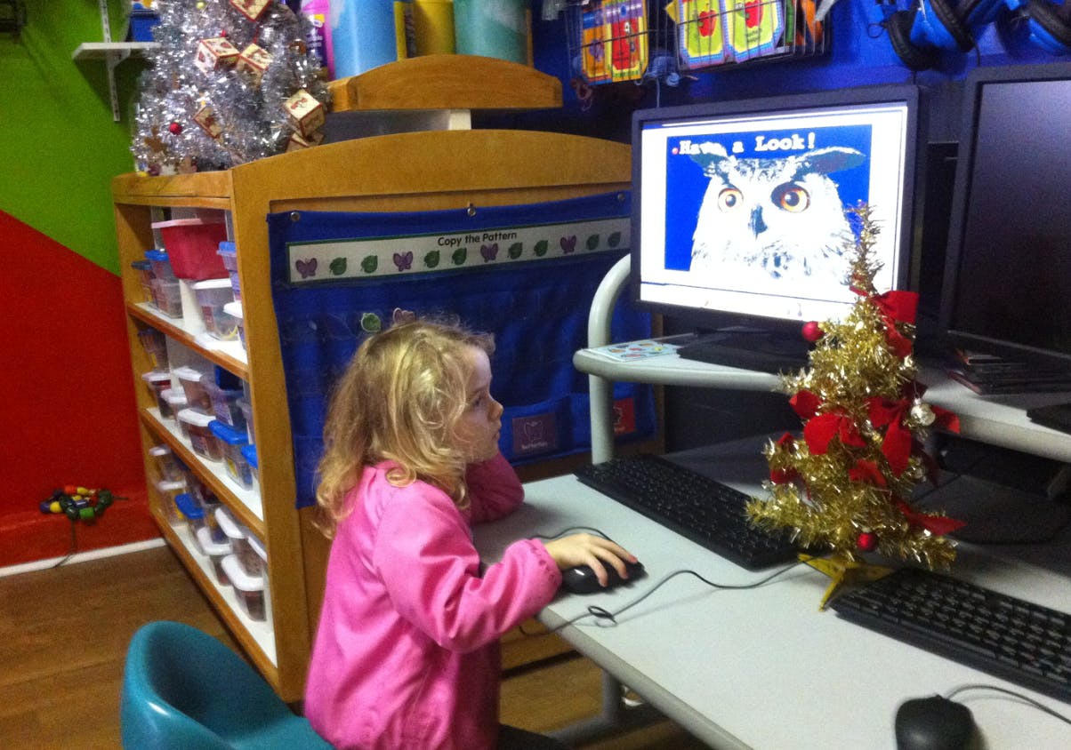 Child using a computer mouse, looking at a screen with an owl image