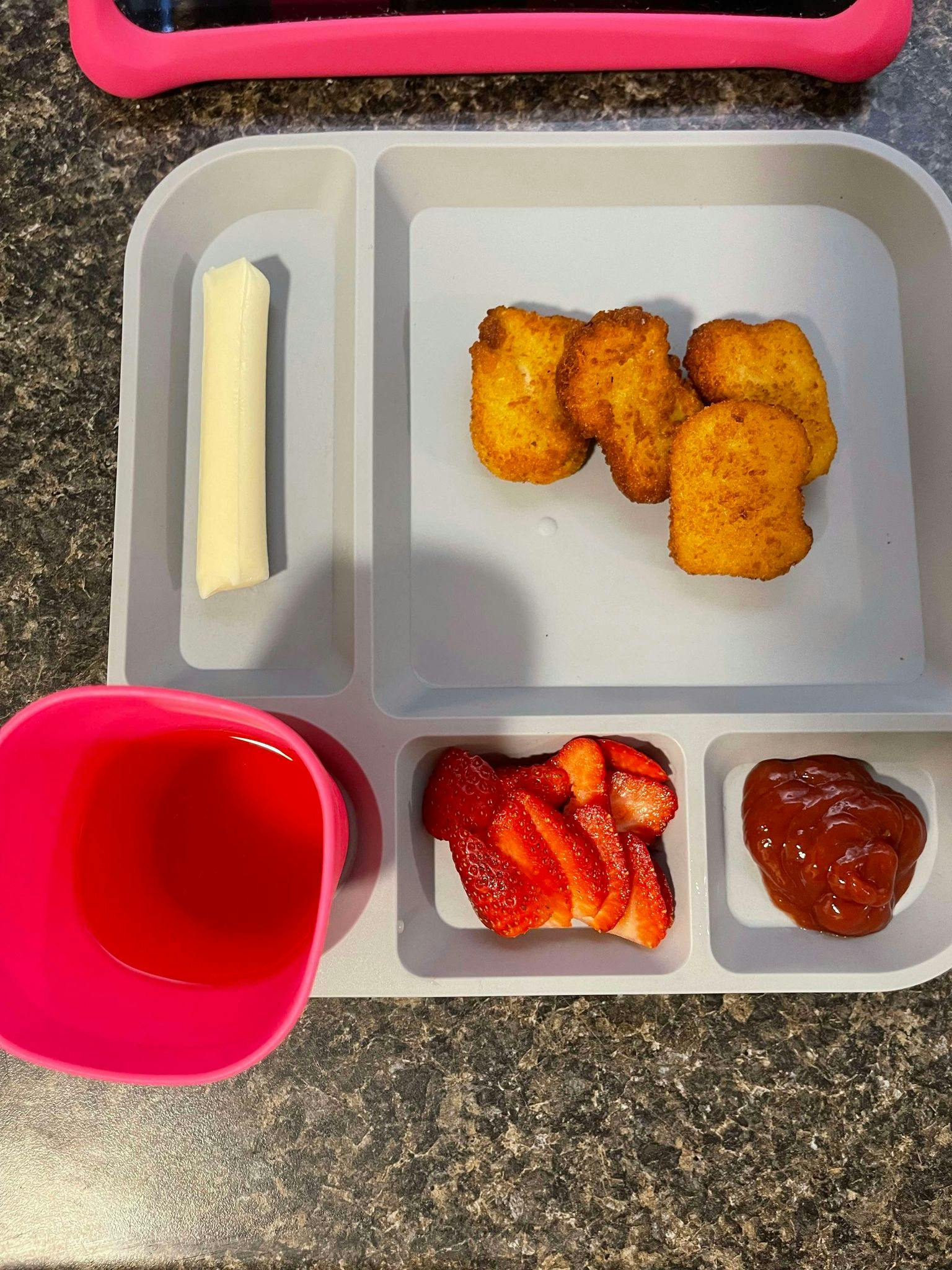 A divided plate with chicken nuggets, string cheese, sliced strawberries, and ketchup