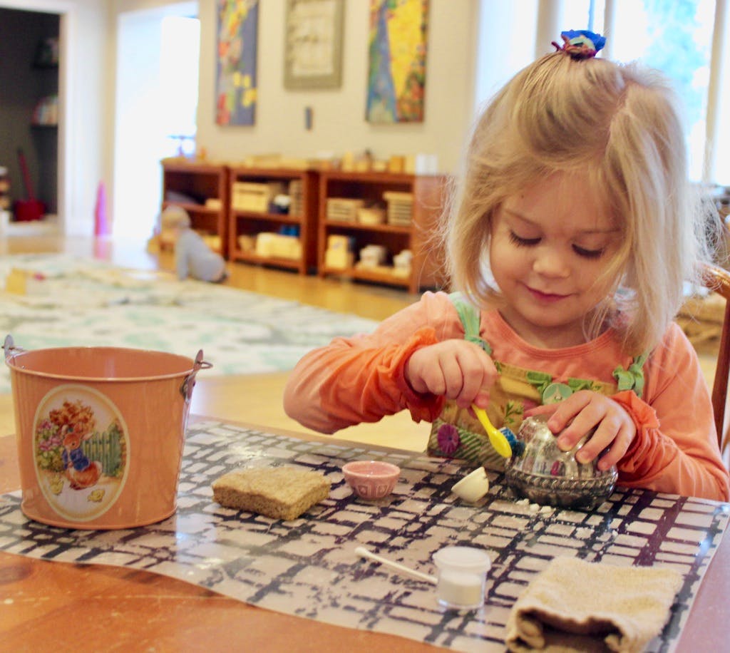 Child cleaning a small metal object with a brush at a table