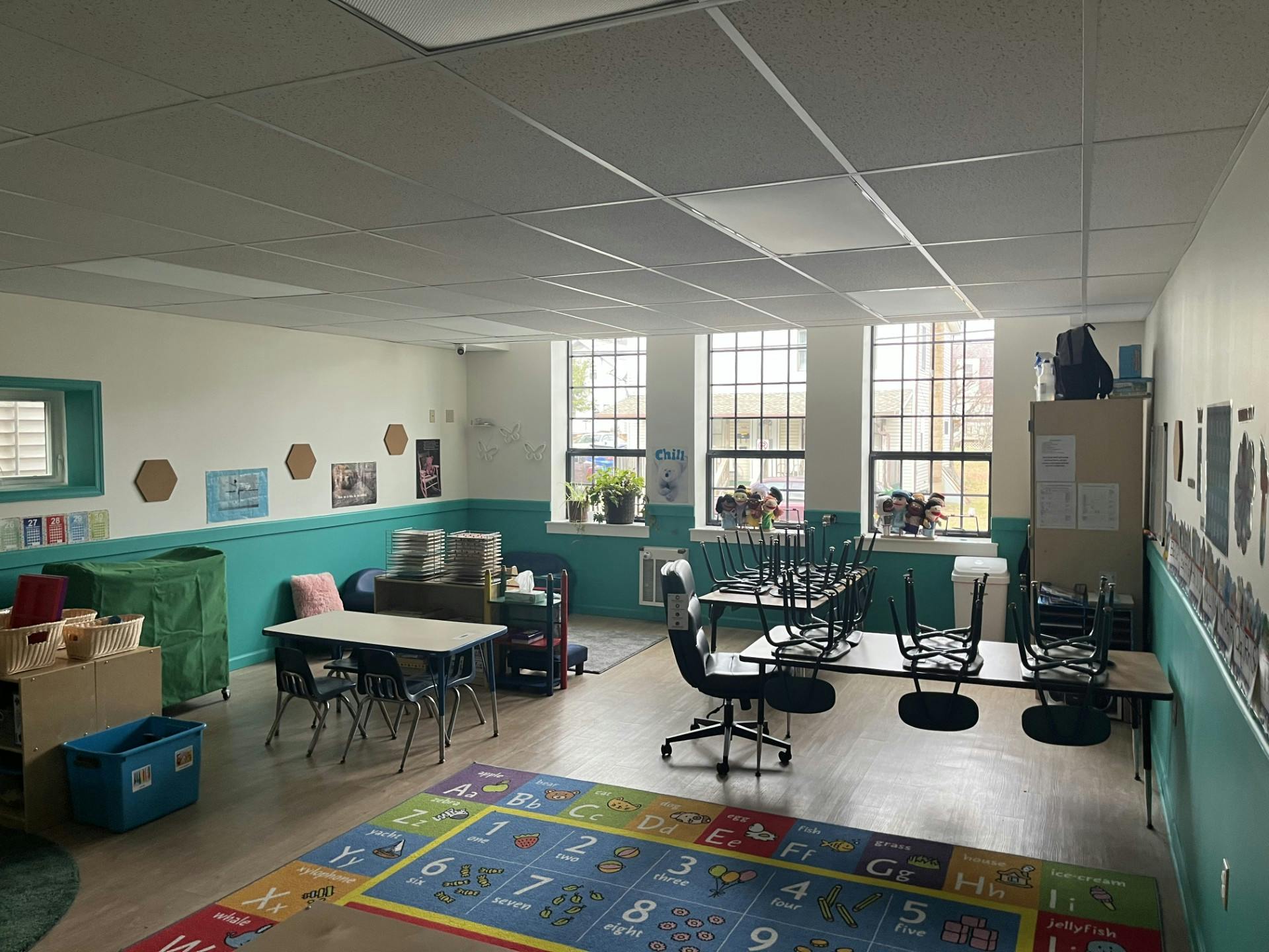 Empty classroom with tables, chairs, and a colorful alphabet rug