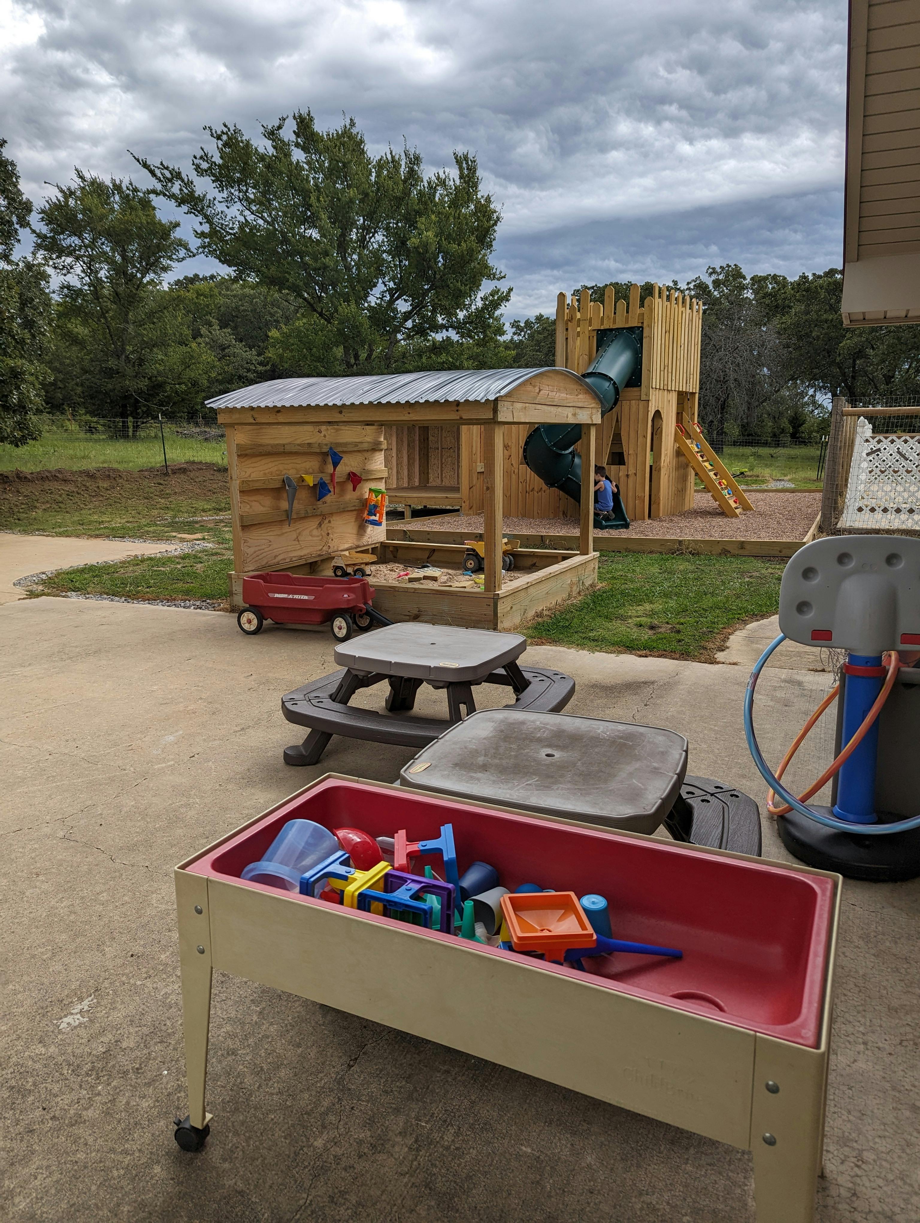 Outdoor playground with wooden playhouse, slide, and sand table with toys