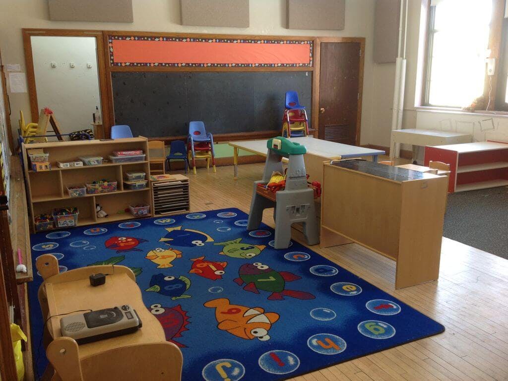 Empty classroom with a blue rug, small chairs, and a chalkboard