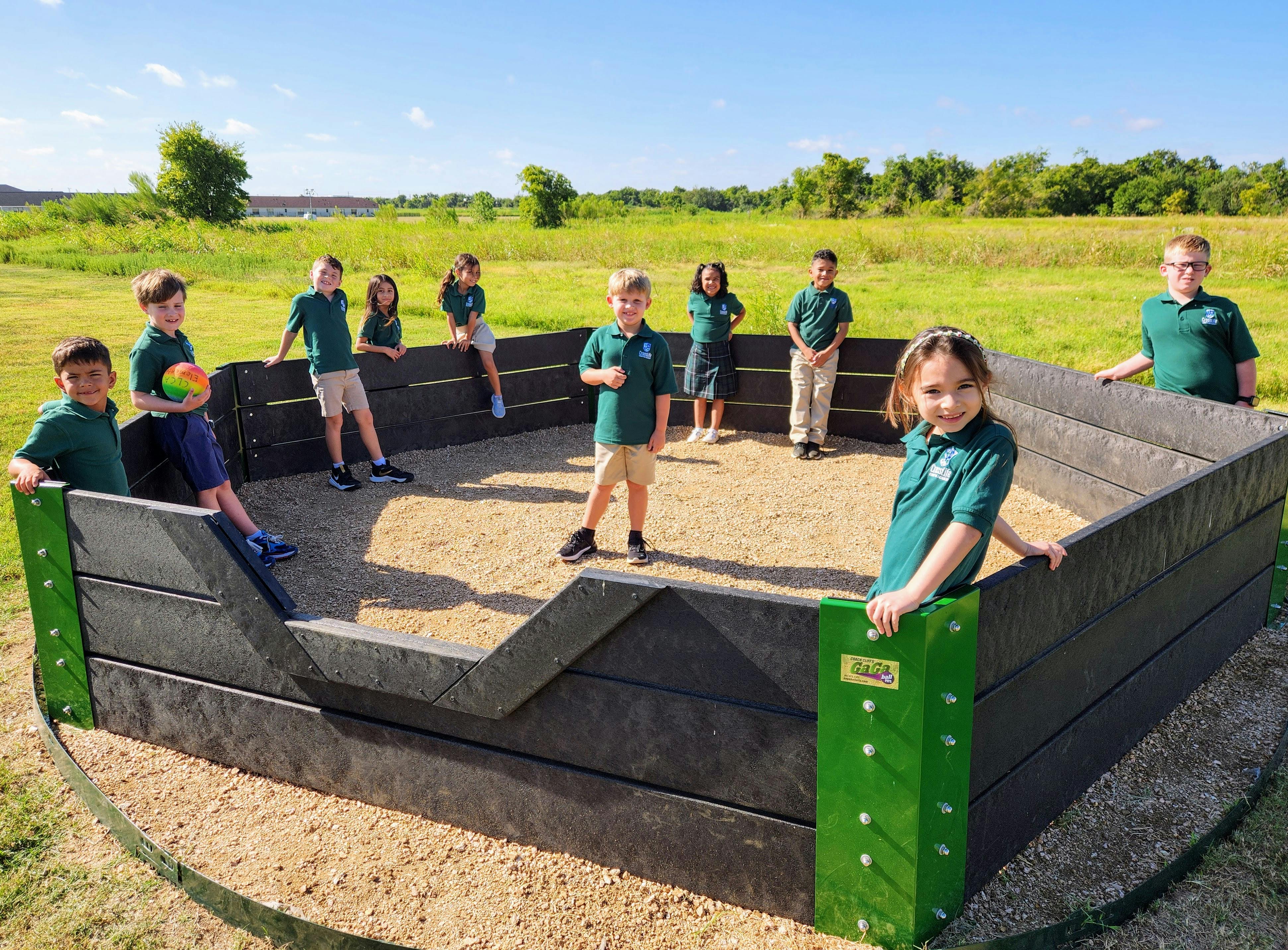 Children in uniforms inside and around a gaga ball pit
