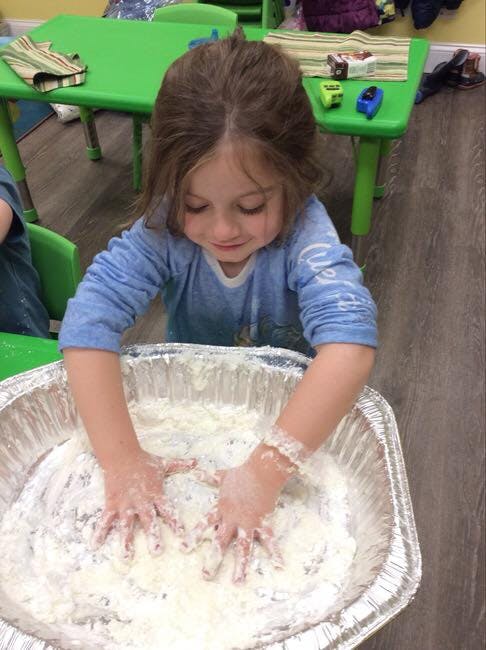 Child playing with hands in a large bowl of white dough