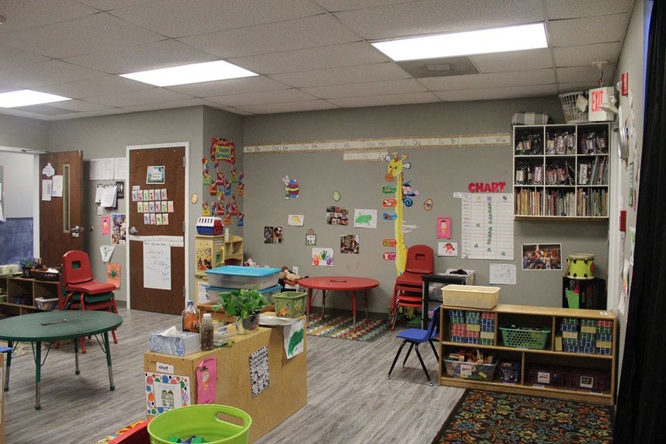 Empty classroom with small tables and chairs, shelves with books and toys