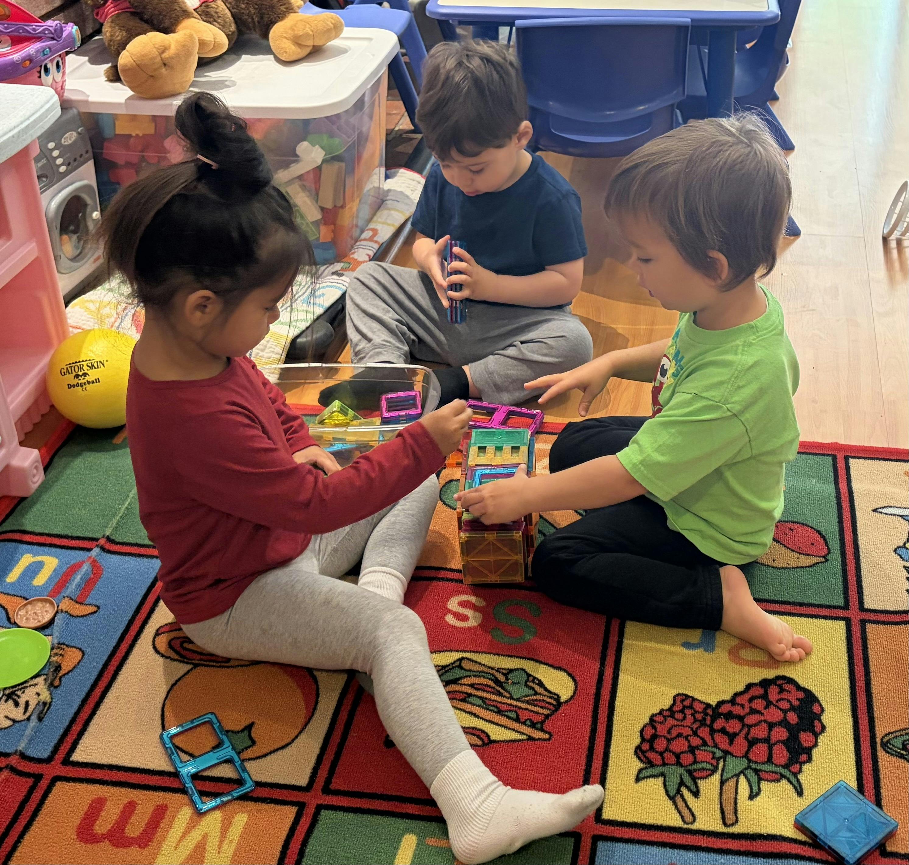 Three children sitting on a colorful rug building with magnetic blocks