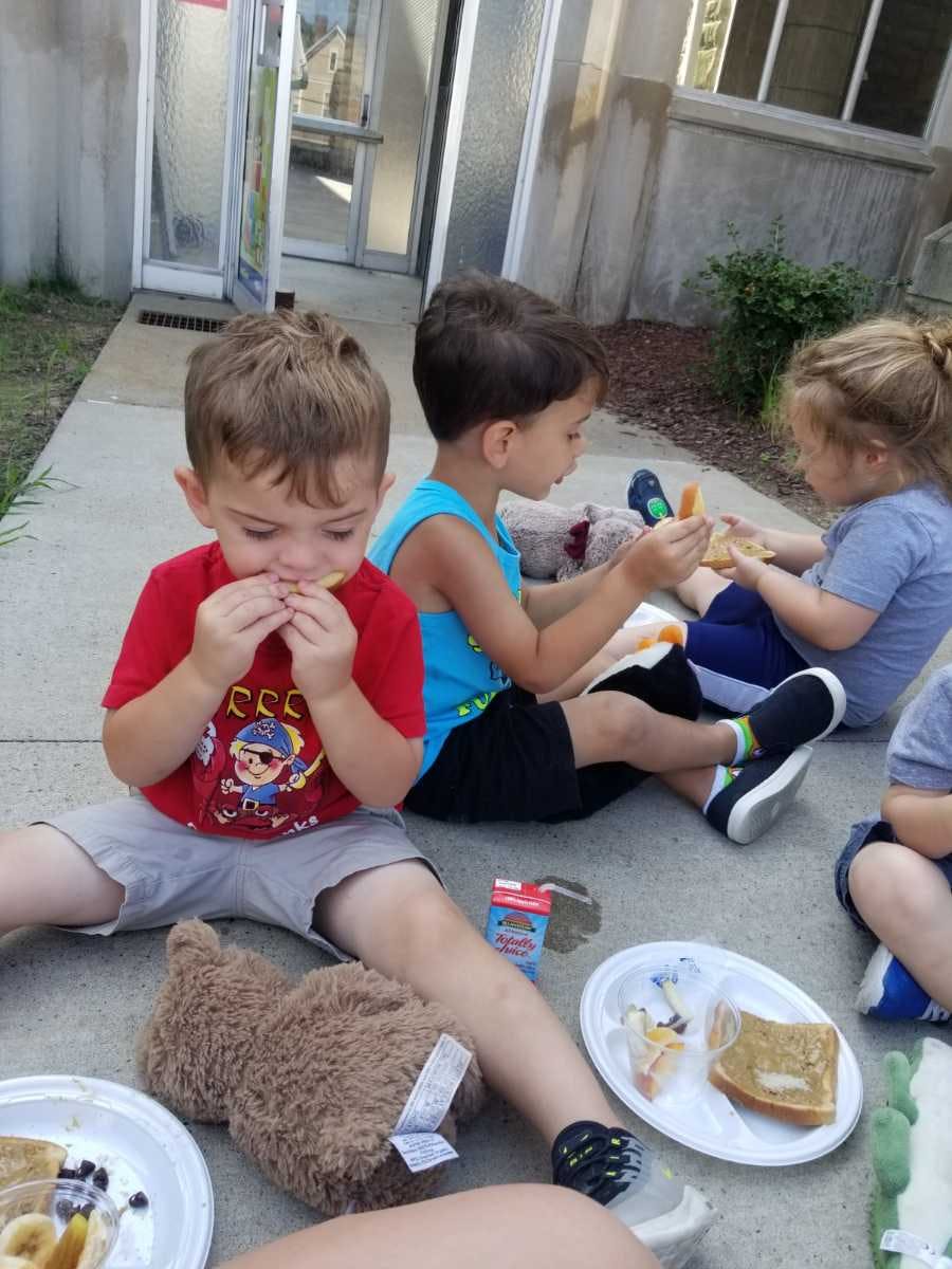 Three children sitting on the ground eating snacks