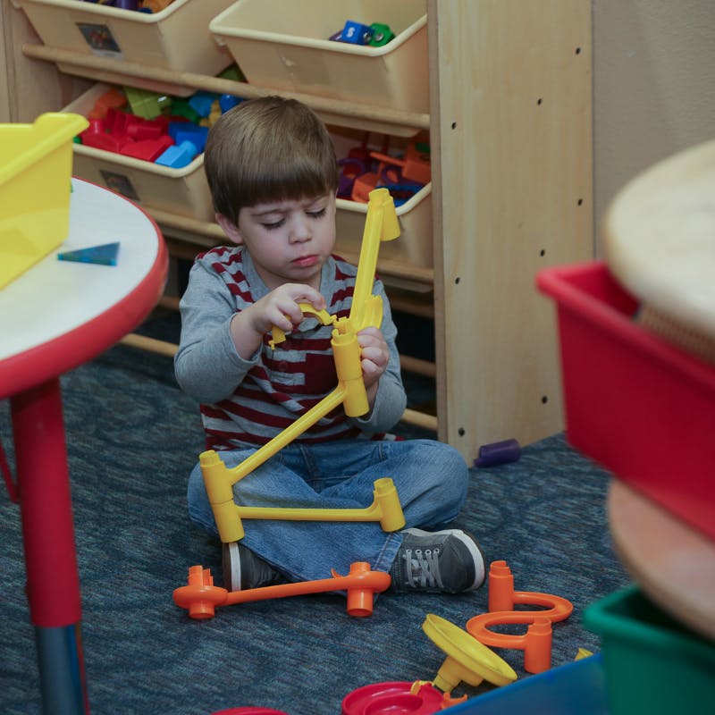 Child sitting on floor playing with yellow and orange building toys