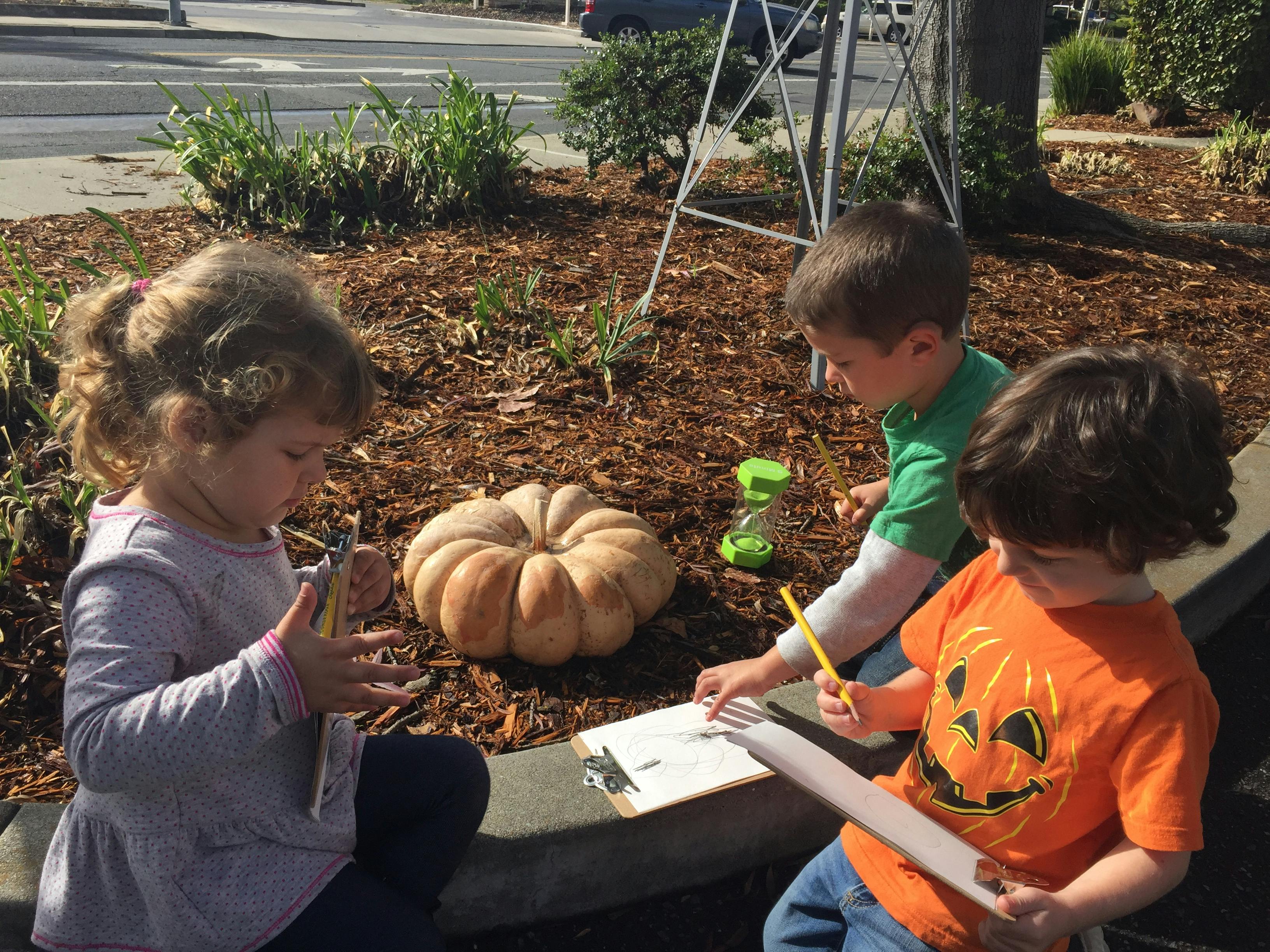 Three children drawing outdoors with a pumpkin