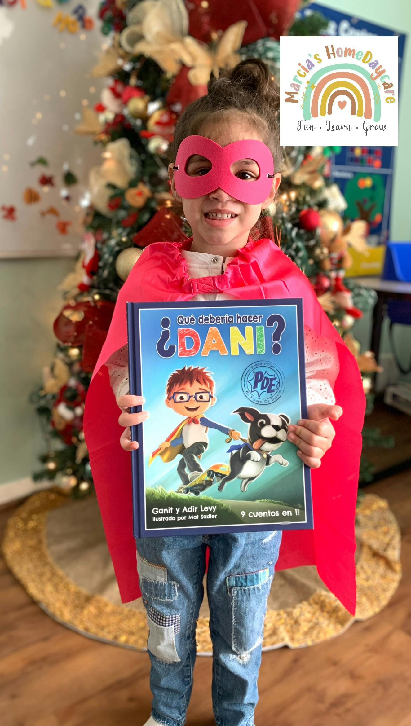 Child in a red cape and mask holding a book titled "¿Que deberia hacer DANI?"