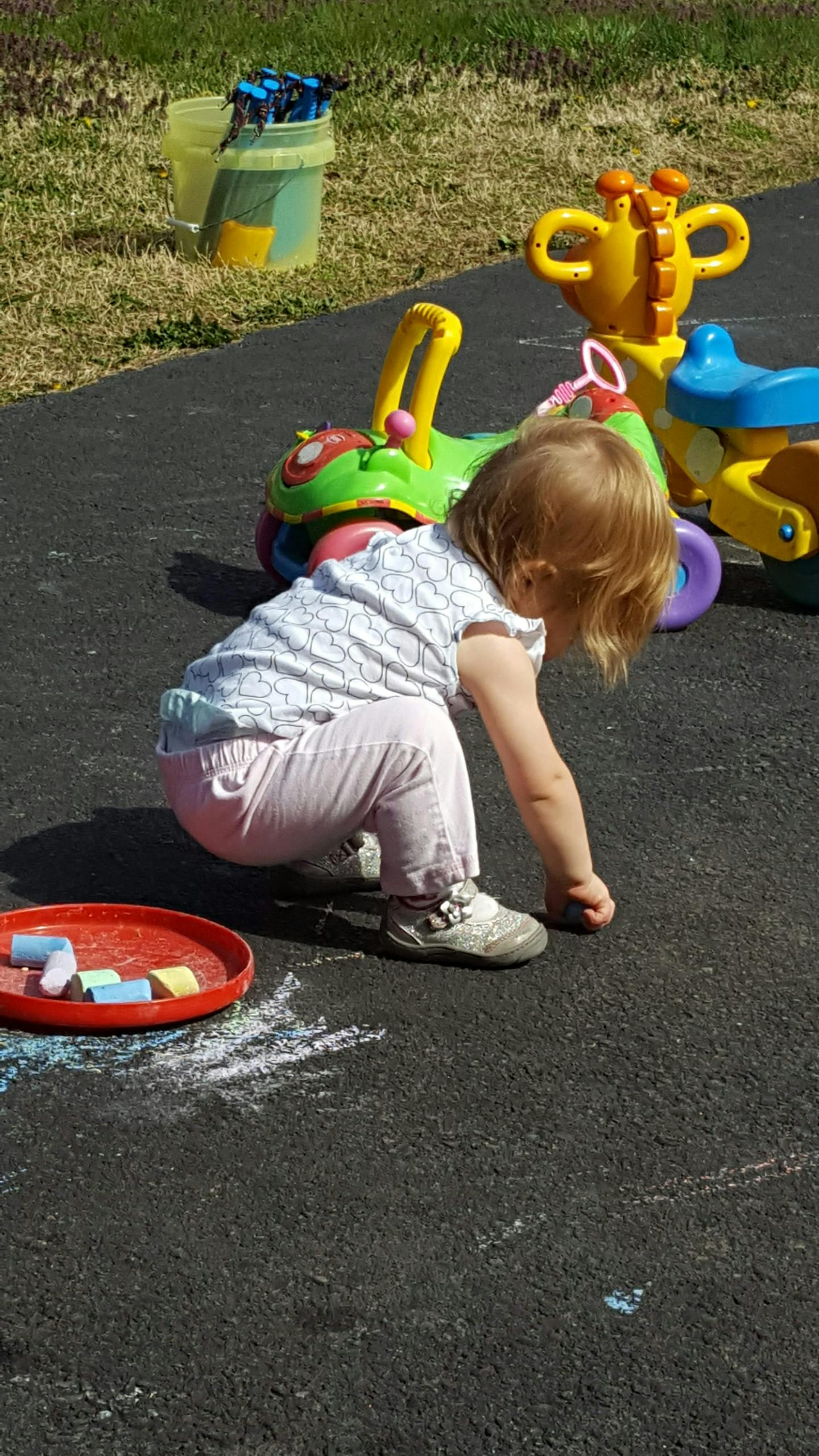 Child crouching on pavement with chalk and toys