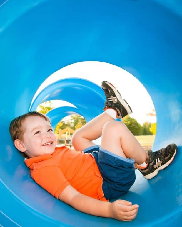Child in an orange shirt and blue shorts lying in a blue tunnel slide