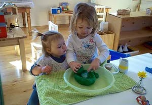 Two children playing with a green toy in a bowl of water