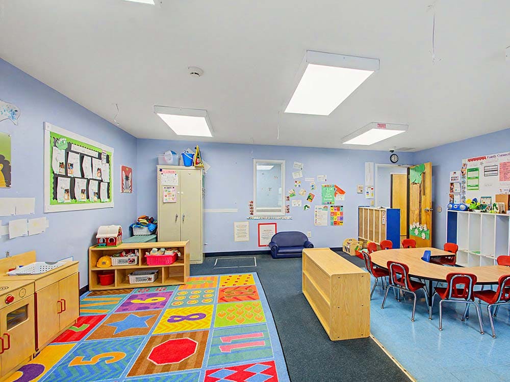 Children's classroom with colorful rug, small tables, and play kitchen