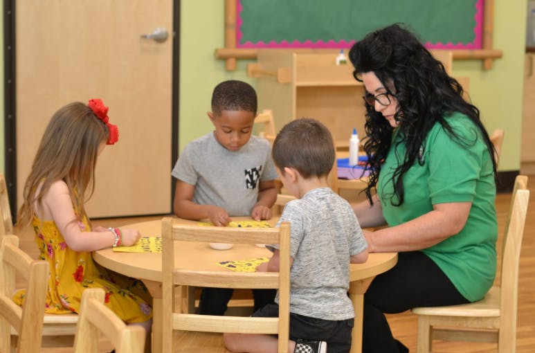 Adult and three children sitting at a table playing with yellow shapes