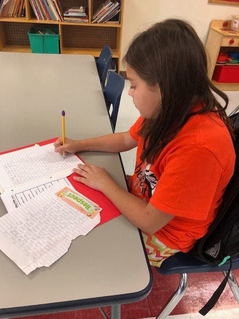 Child writing with a pencil at a desk in a classroom